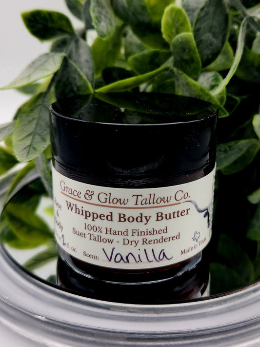 Jar of Grace & Glow Tallow Co. Whipped Body Butter with a vanilla scent, surrounded by green leaves.
